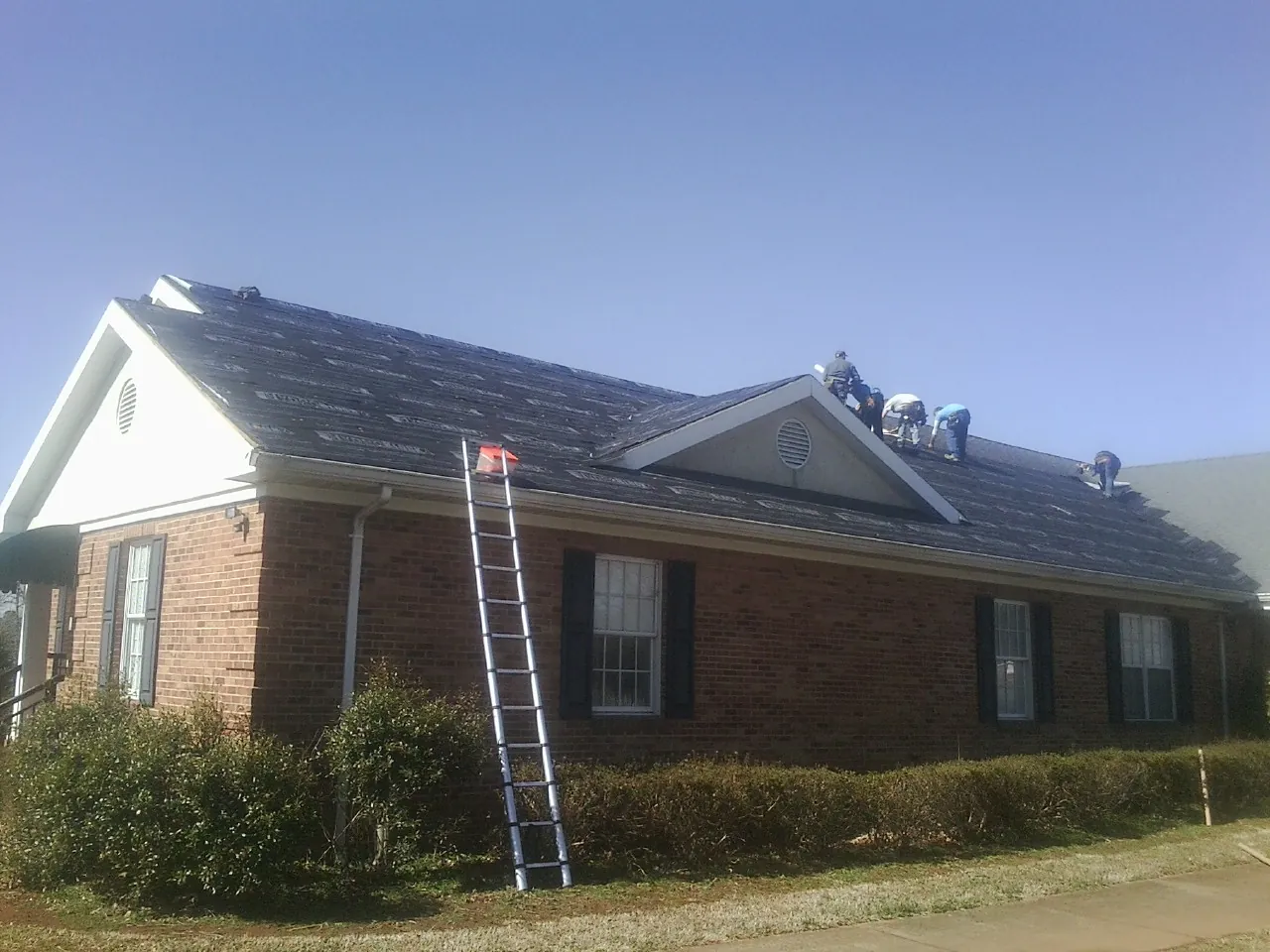 Crew tearing shingles off a brick ranch roof with a ladder set — Emergency Roof Repair work by our crew in Crystal Lake
