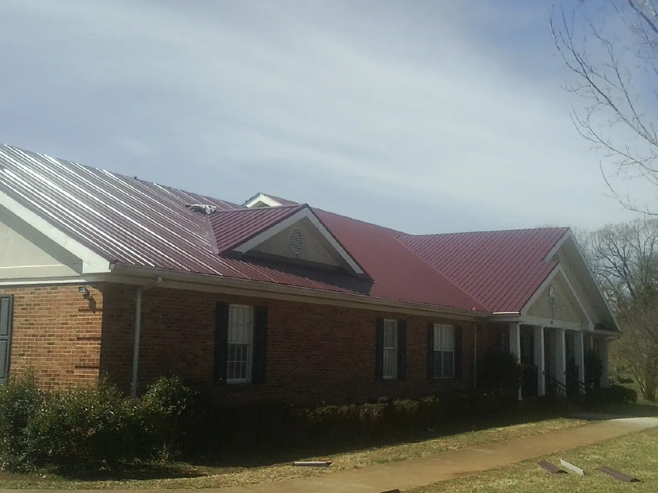 Red metal roof with gabled entries on a long brick building, from a Hail Damage Roof Repair job in Crystal Lake