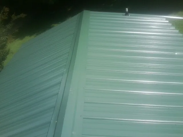 New green metal panels meeting at the ridge of a roof — Flat Roof Repair work by our crew in Crystal Lake