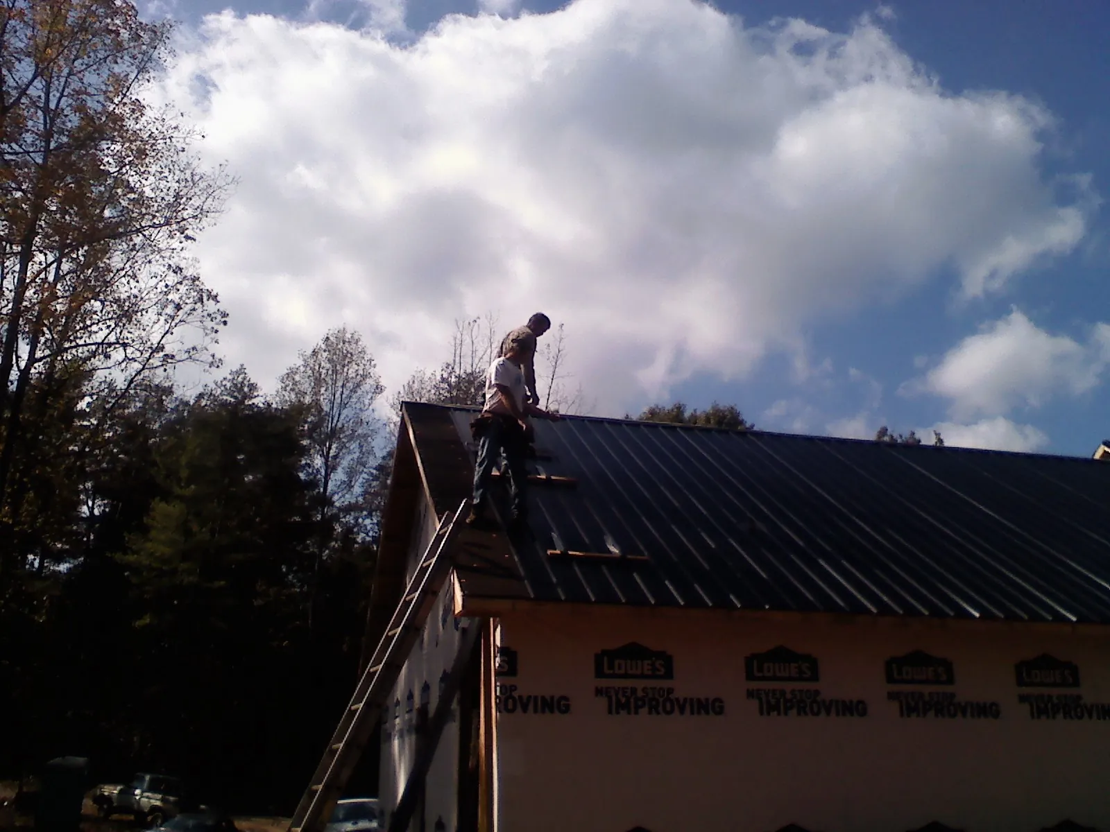 Roofer fastening dark metal panels high against a cloudy sky, from a Roof Inspection job in Crystal Lake