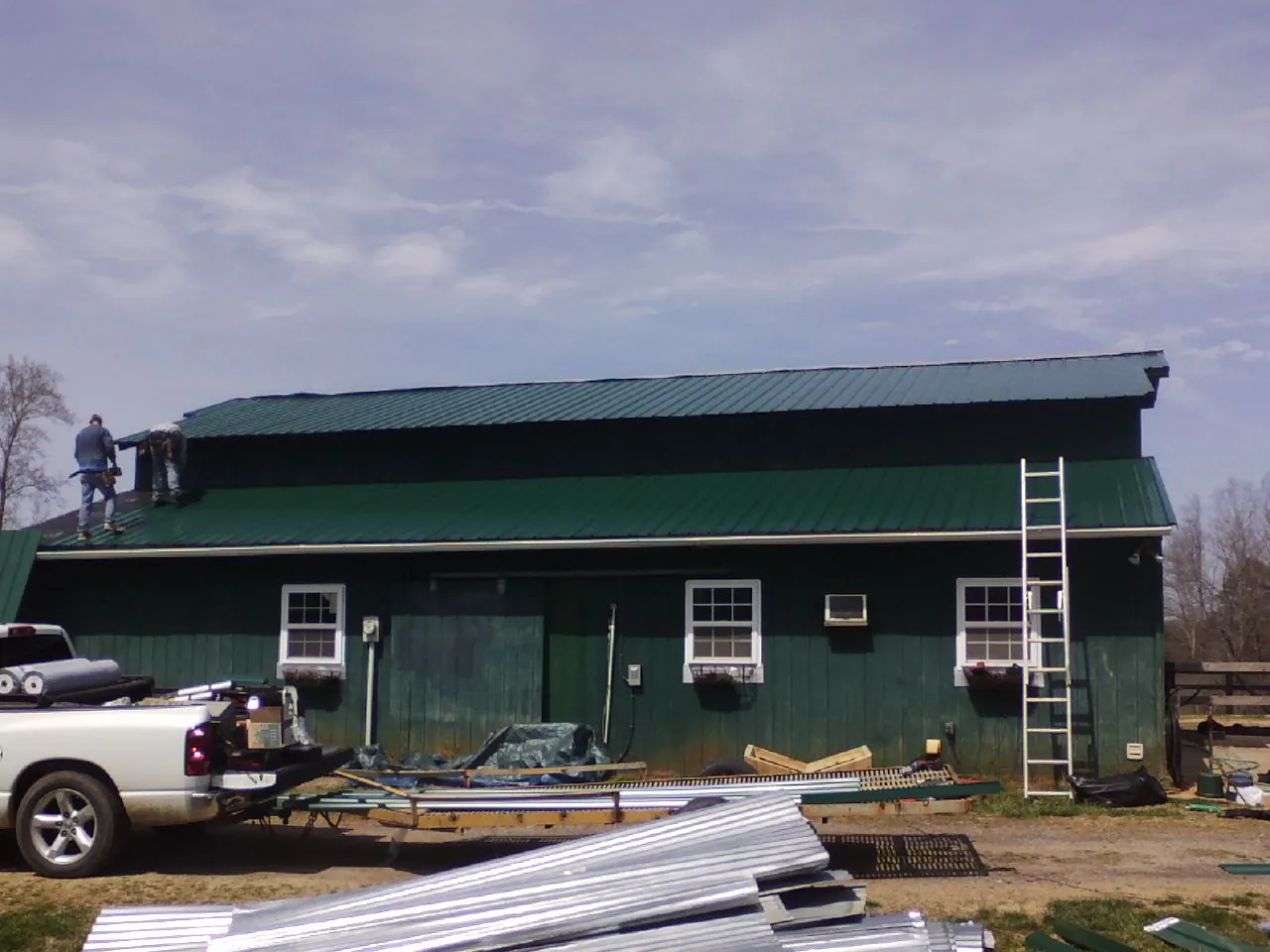 Crew installing green metal roofing on a large green barn in Crystal Lake