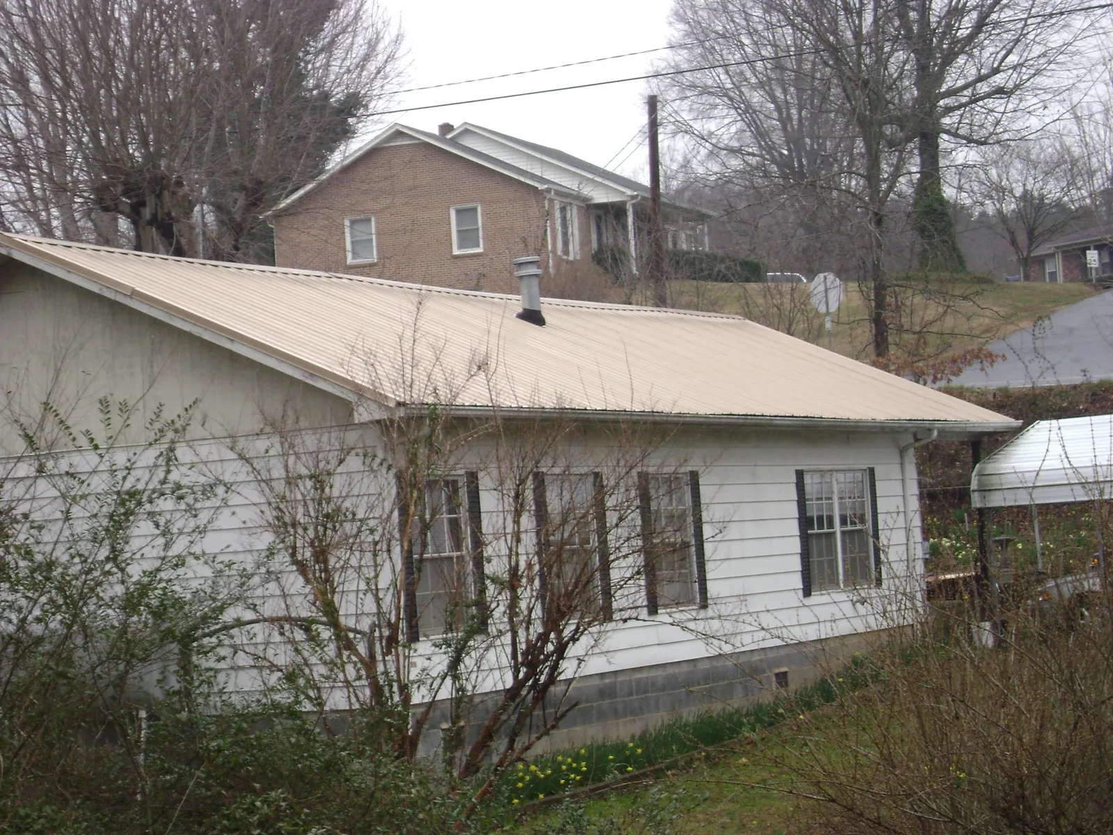 Tan metal roof on a white sided house set into a hillside — Commercial Roofing by Roofing Brothers in Crystal Lake